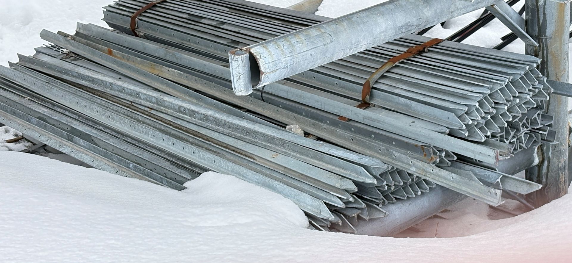 Des tuyaux métalliques argentés empilés et liés par du fil de fer sur une surface enneigée