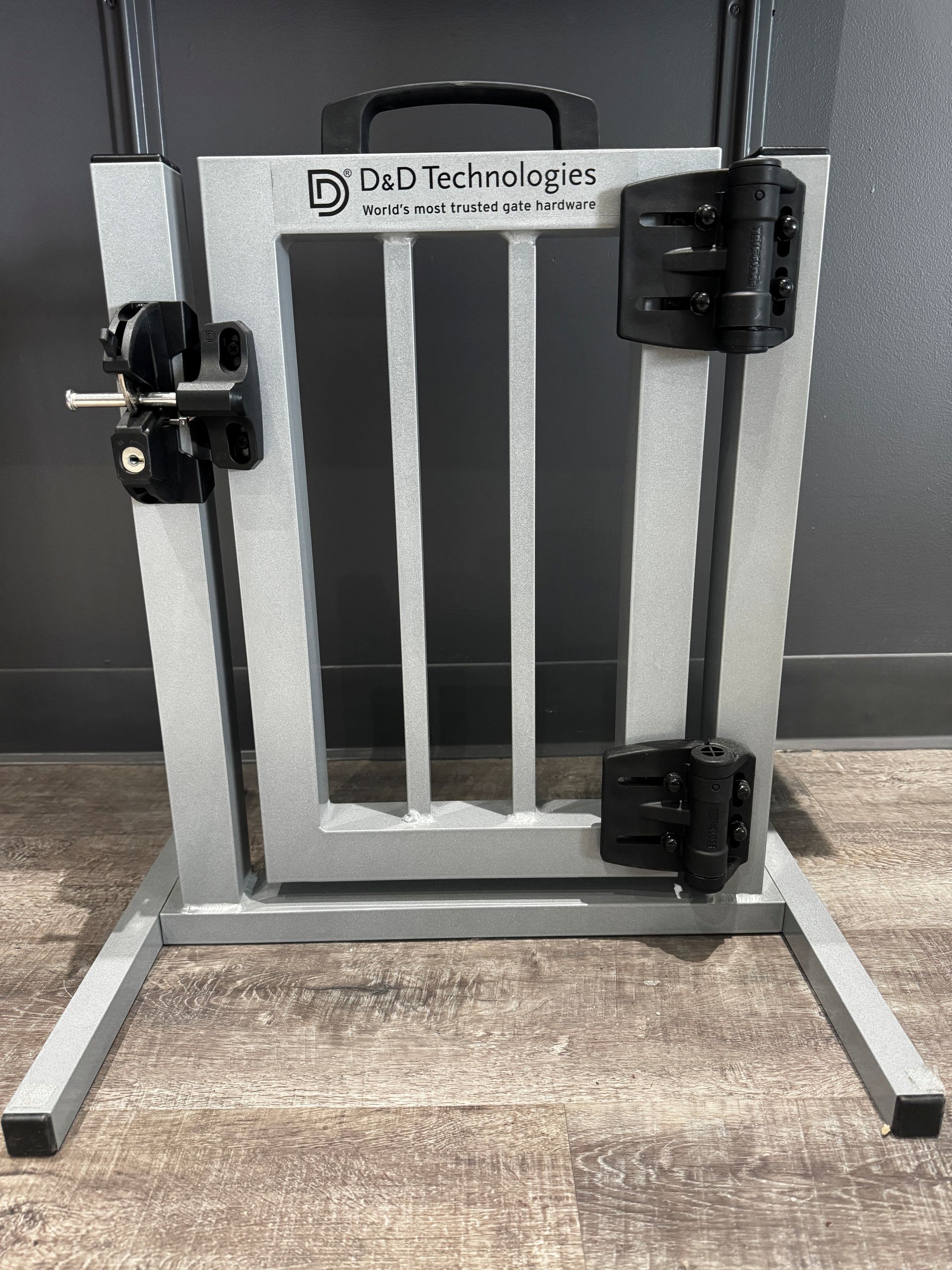 Barrière pour animaux en métal gris avec loquets noirs, posée au sol contre un mur.