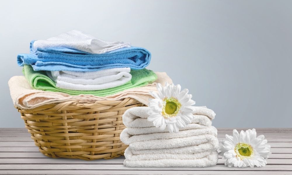 A wicker basket filled with towels and flowers on a wooden table.