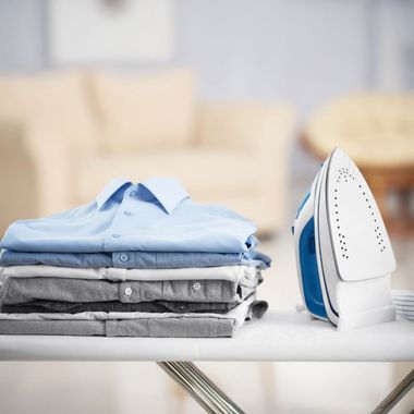 A stack of shirts sits on an ironing board next to an iron