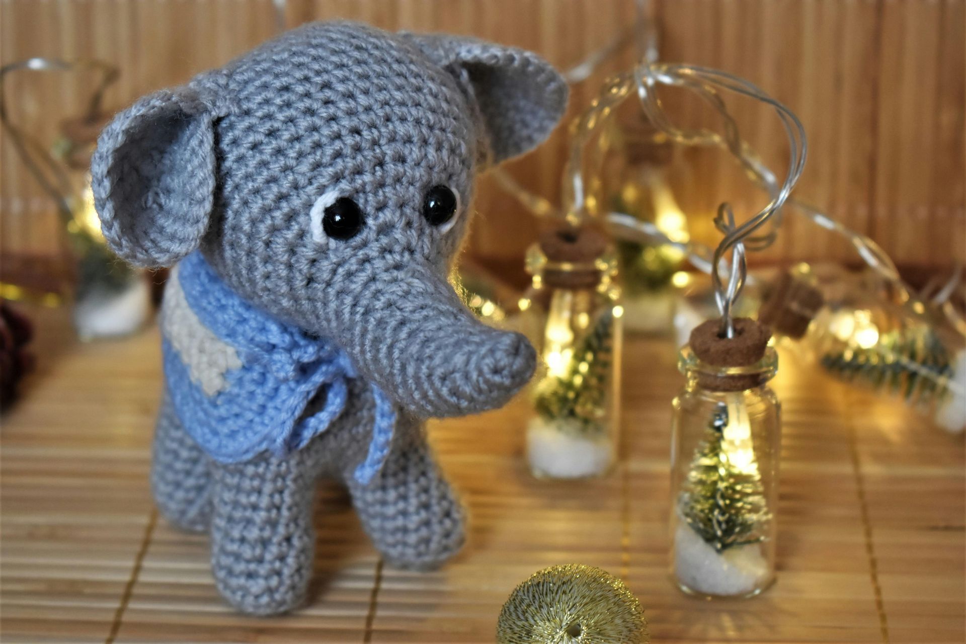 A crocheted elephant is standing next to a string of christmas lights.
