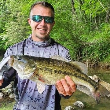 a man wearing sunglasses is holding a large bass in his hands .