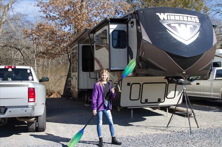 a young girl is holding a paddle in front of a camper trailer .