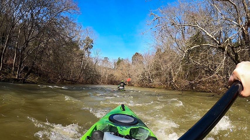 a person is paddling a green kayak down a river .