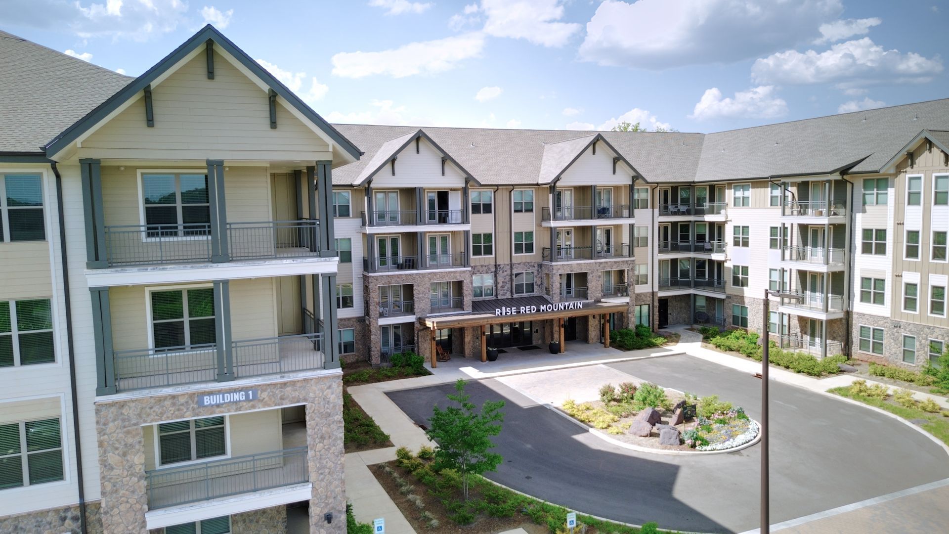 Apartment complex with beige and white buildings surrounding a landscaped courtyard and driveway