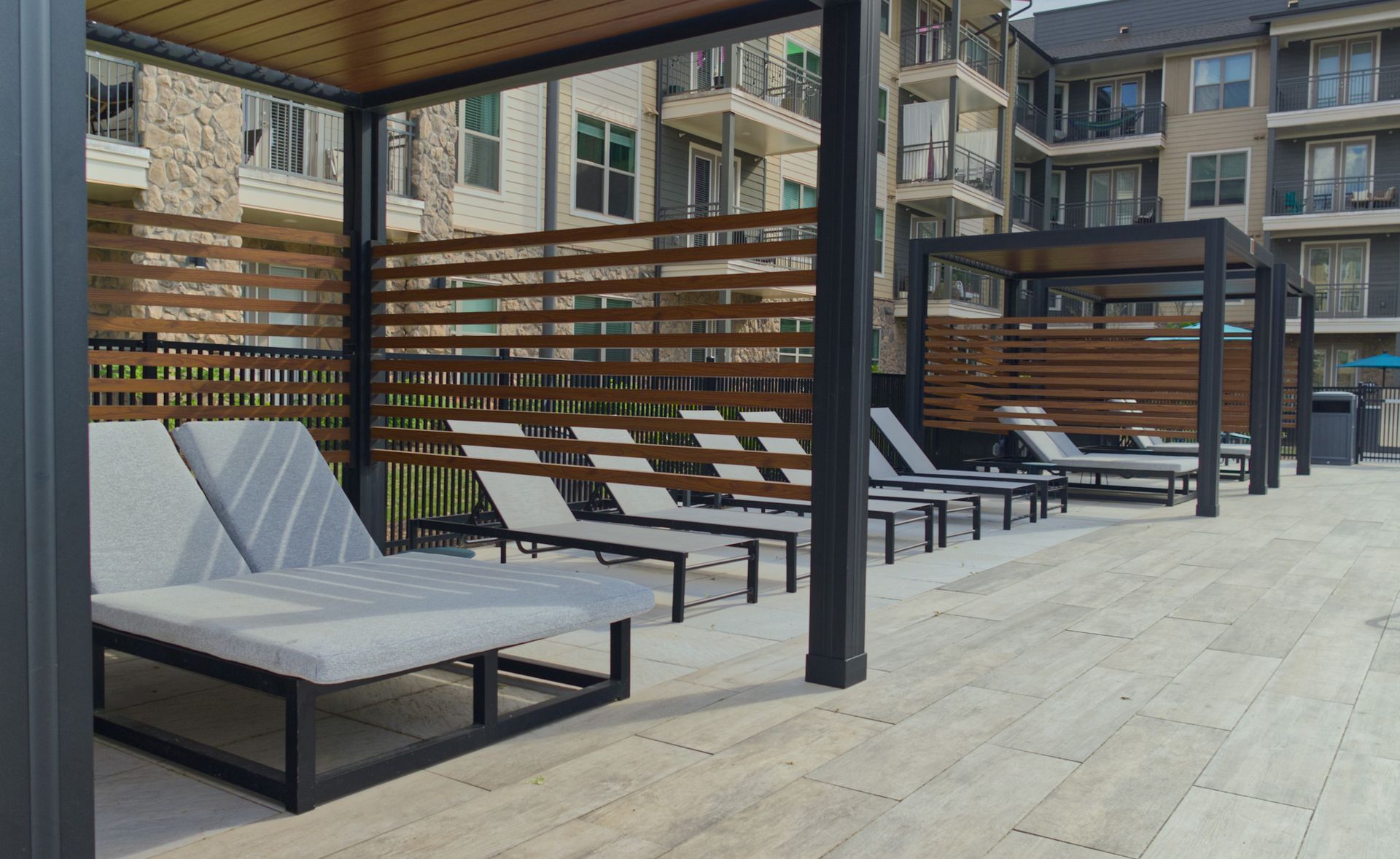 Modern outdoor patio with lounge chairs, wooden slat screens, and a covered seating area on a boardwalk.
