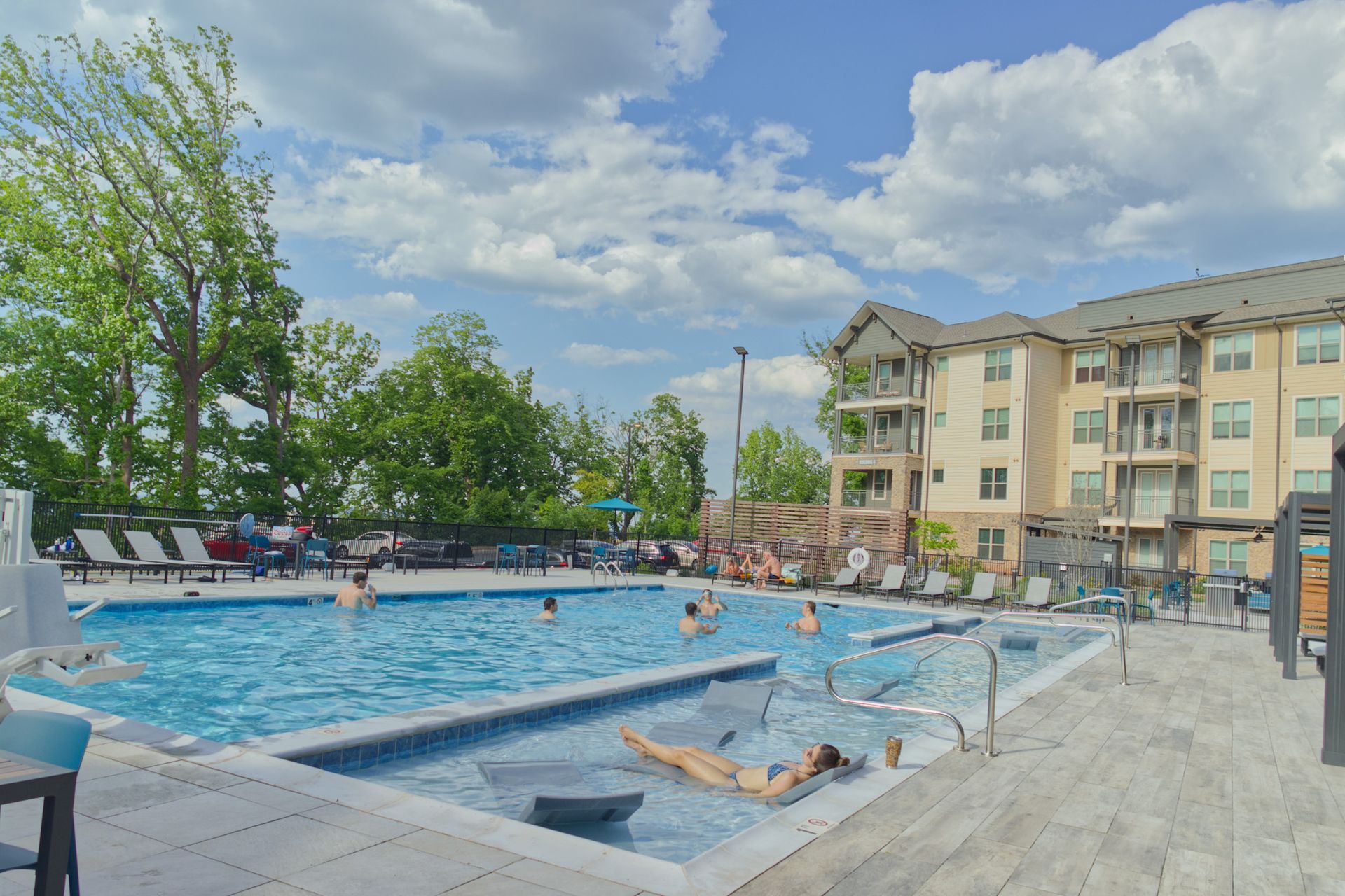 Outdoor apartment pool with swimmers, lounge chairs, and a cloudy sky