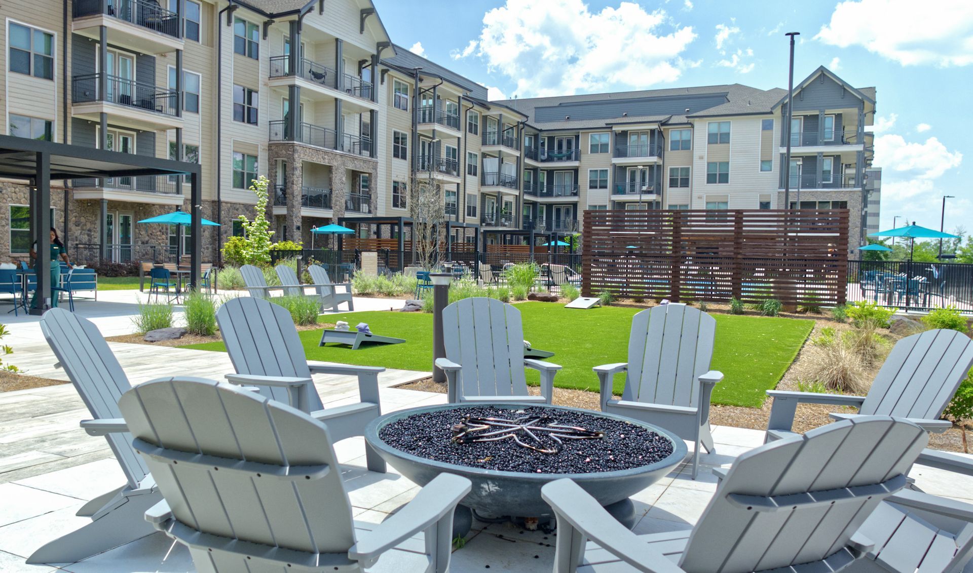 Apartment courtyard with fire pit chairs, picnic tables, green lawn, and modern buildings in the background