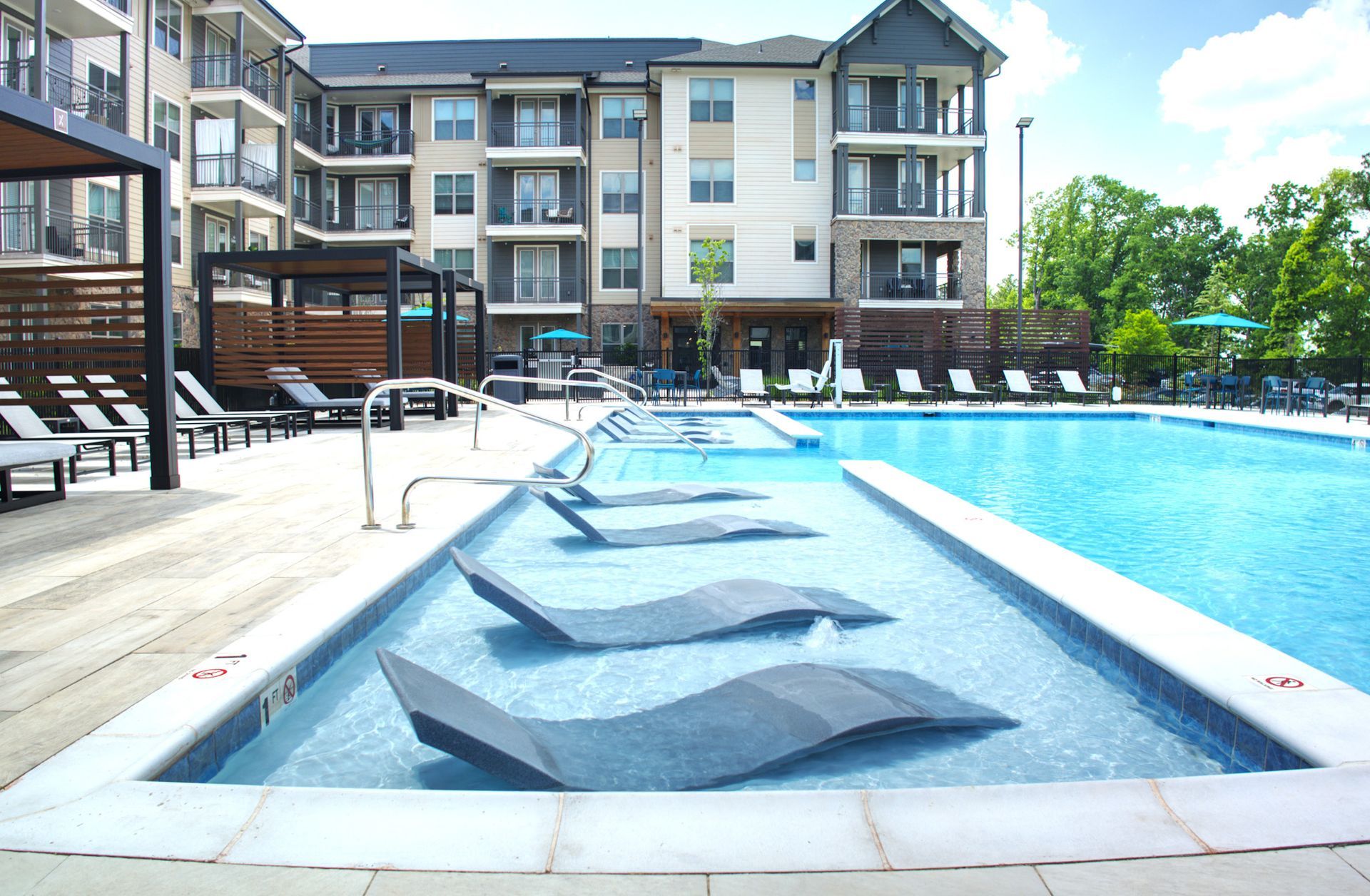 Apartment pool with a shallow sun shelf and lounge chairs beside the water