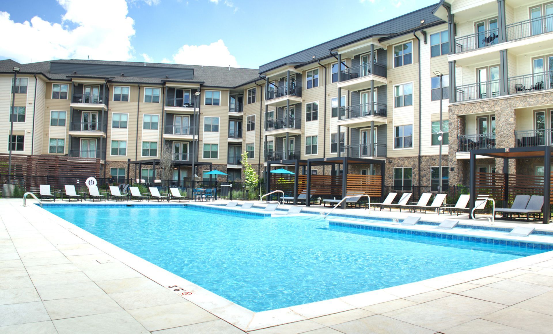 Outdoor apartment courtyard with a blue swimming pool and lounge chairs in front of multi-story buildings