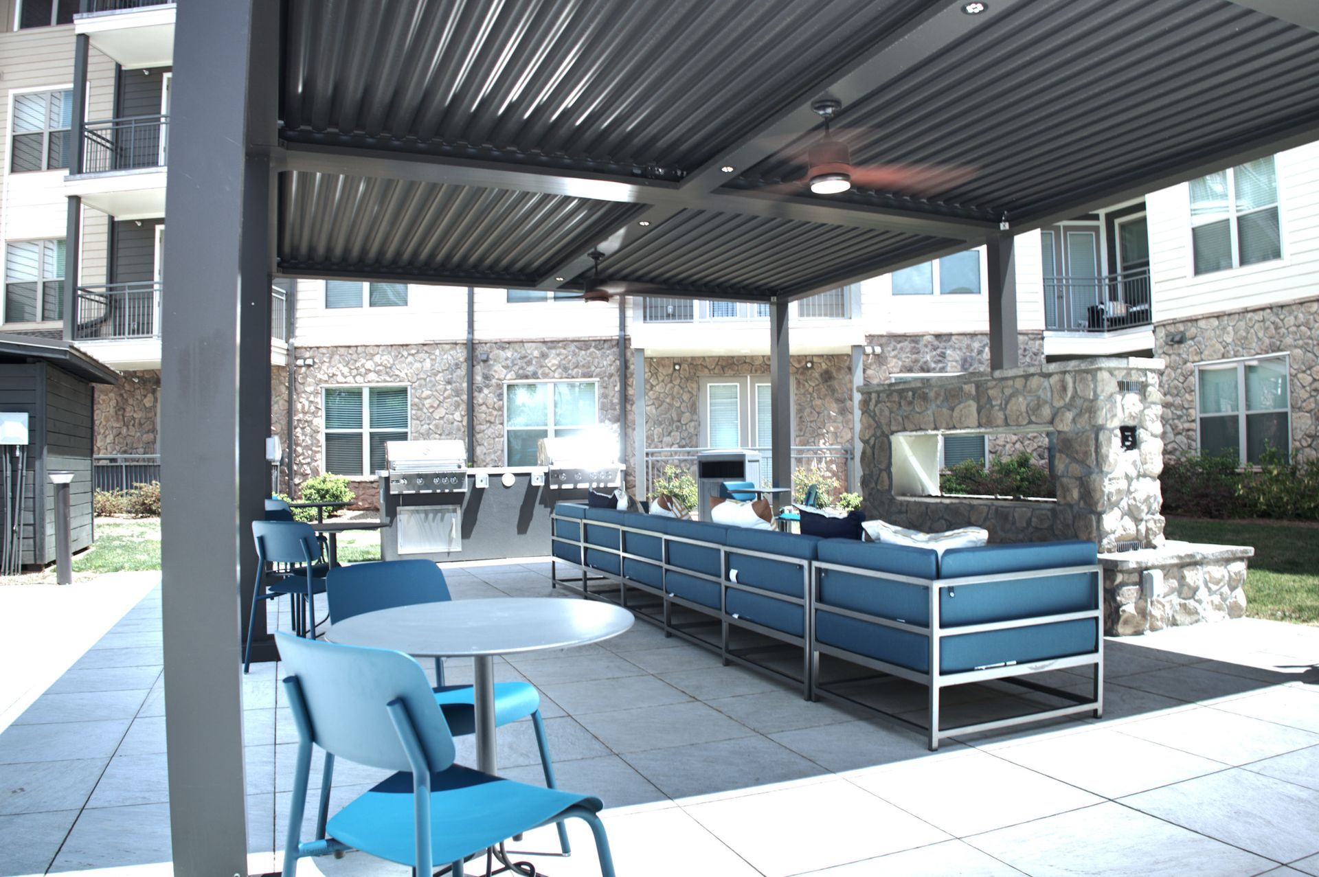 Covered apartment courtyard seating area with blue benches and chairs under a metal canopy