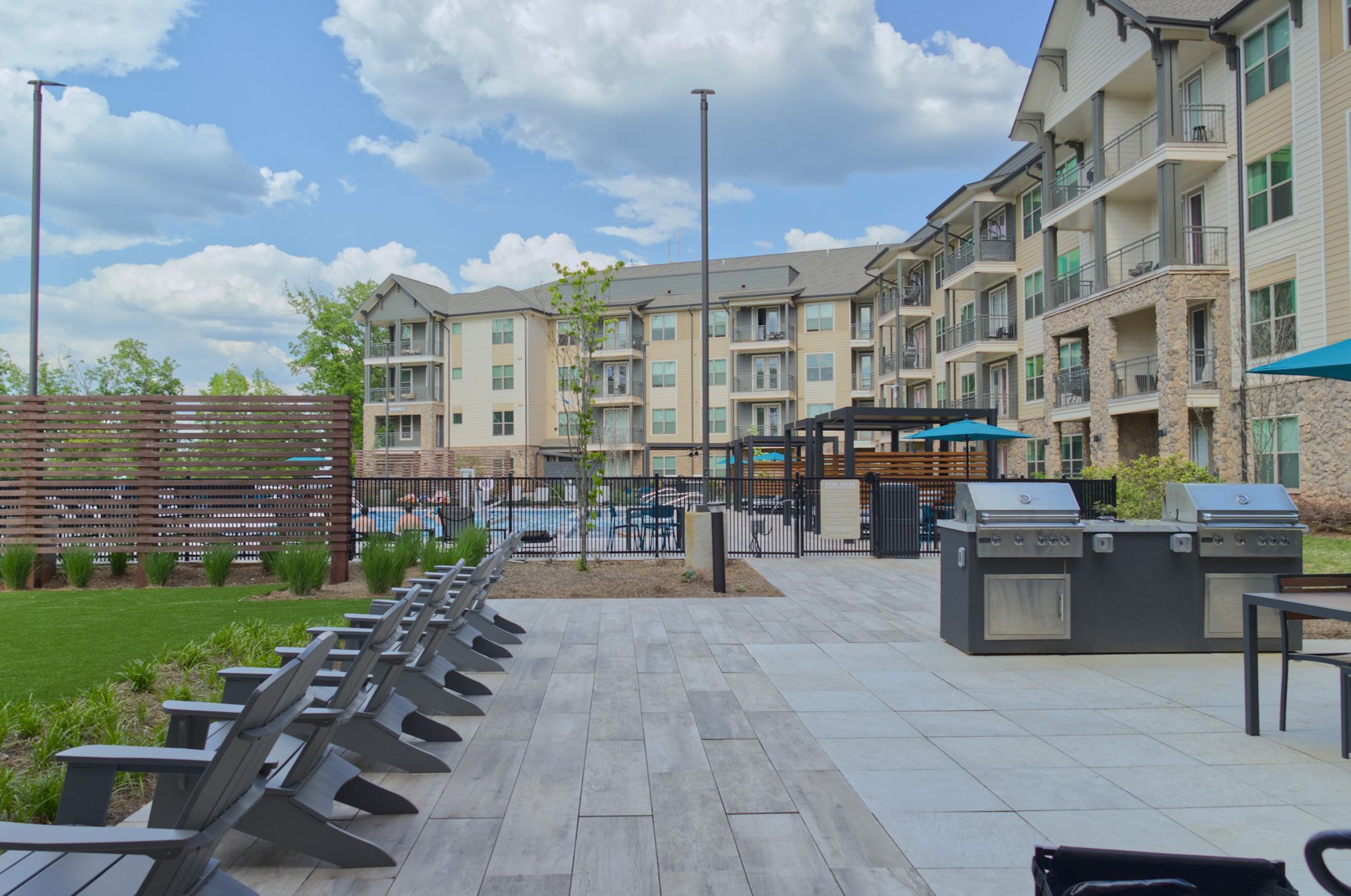Courtyard patio with lounge chairs, grill stations, and apartment buildings under a cloudy sky