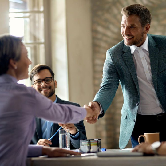Business meeting with two people shaking hands across a conference table, others smiling in the background