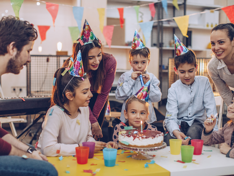 People at a birthday party, gathered around a cake with a candle, celebrating in a room with decorations.
