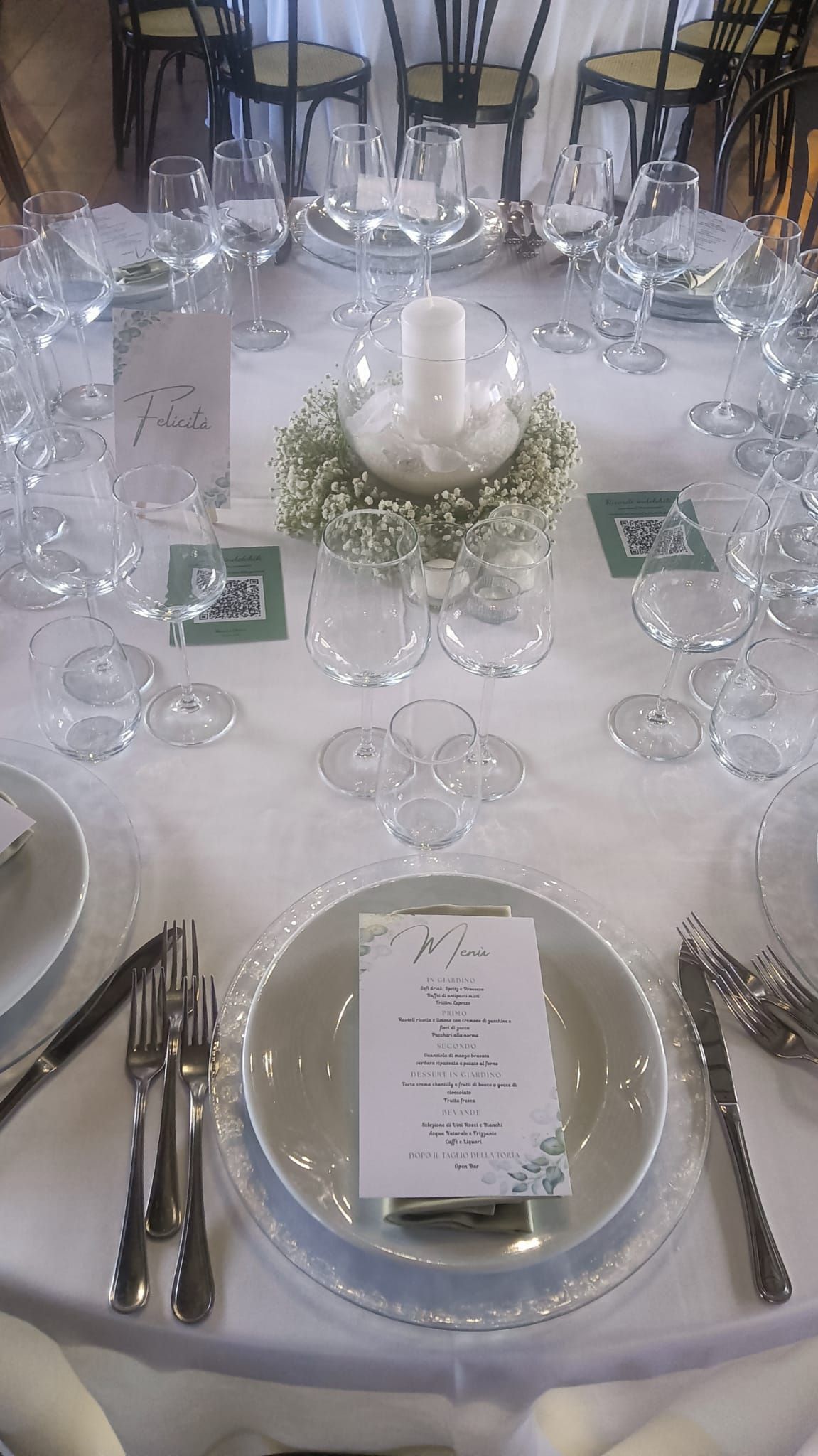 Tavolo da pranzo formale apparecchiato per un matrimonio con tovaglia bianca, fiori, bicchieri e menù.