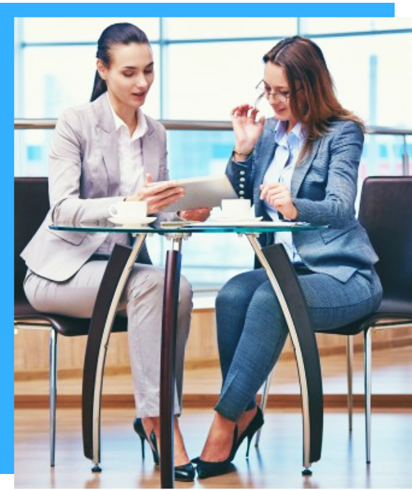 Two women are sitting at a table looking at a tablet.
