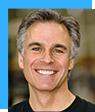 A man with gray hair is smiling and wearing a black shirt.
