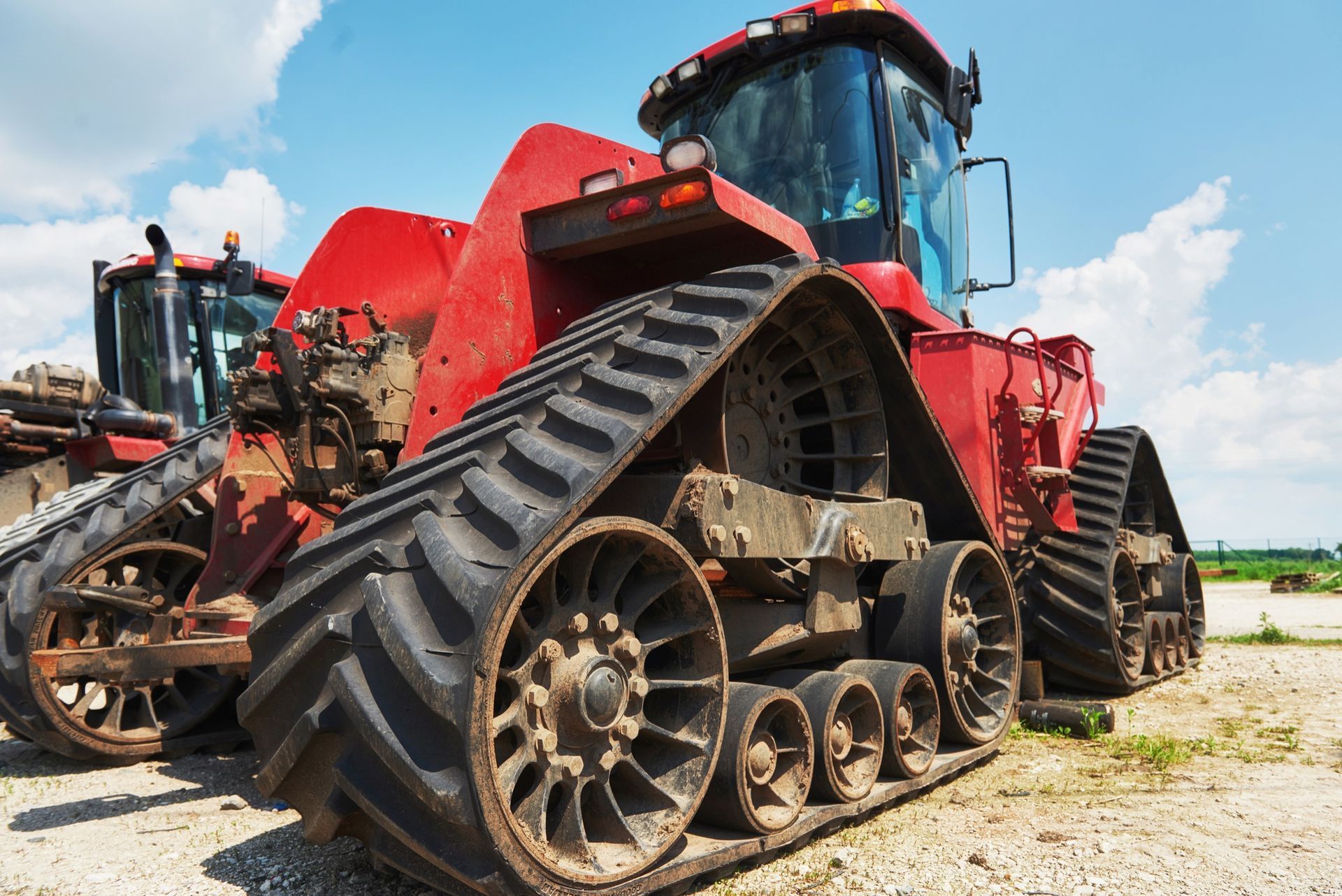 Red tractor with tracks, parked on a sunny day. Another tractor visible in background.
