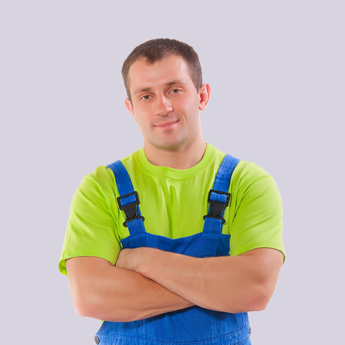 Man in blue overalls and green shirt with arms crossed, smiling.