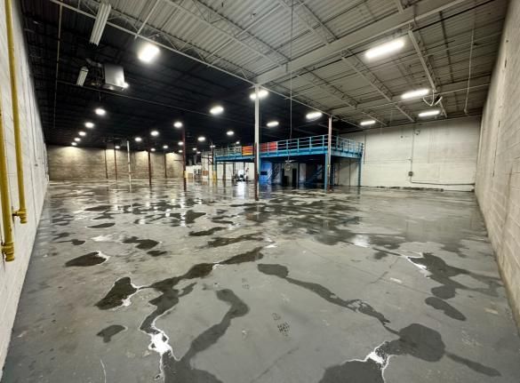 Empty warehouse with puddles on the floor, overhead lights, and a mezzanine level.