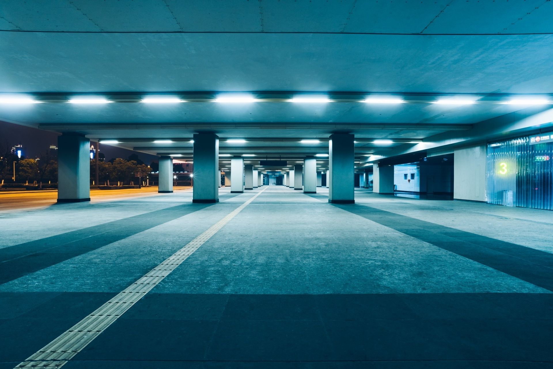 Underpass lit by rows of lights at night. Concrete columns and floor create a receding perspective.