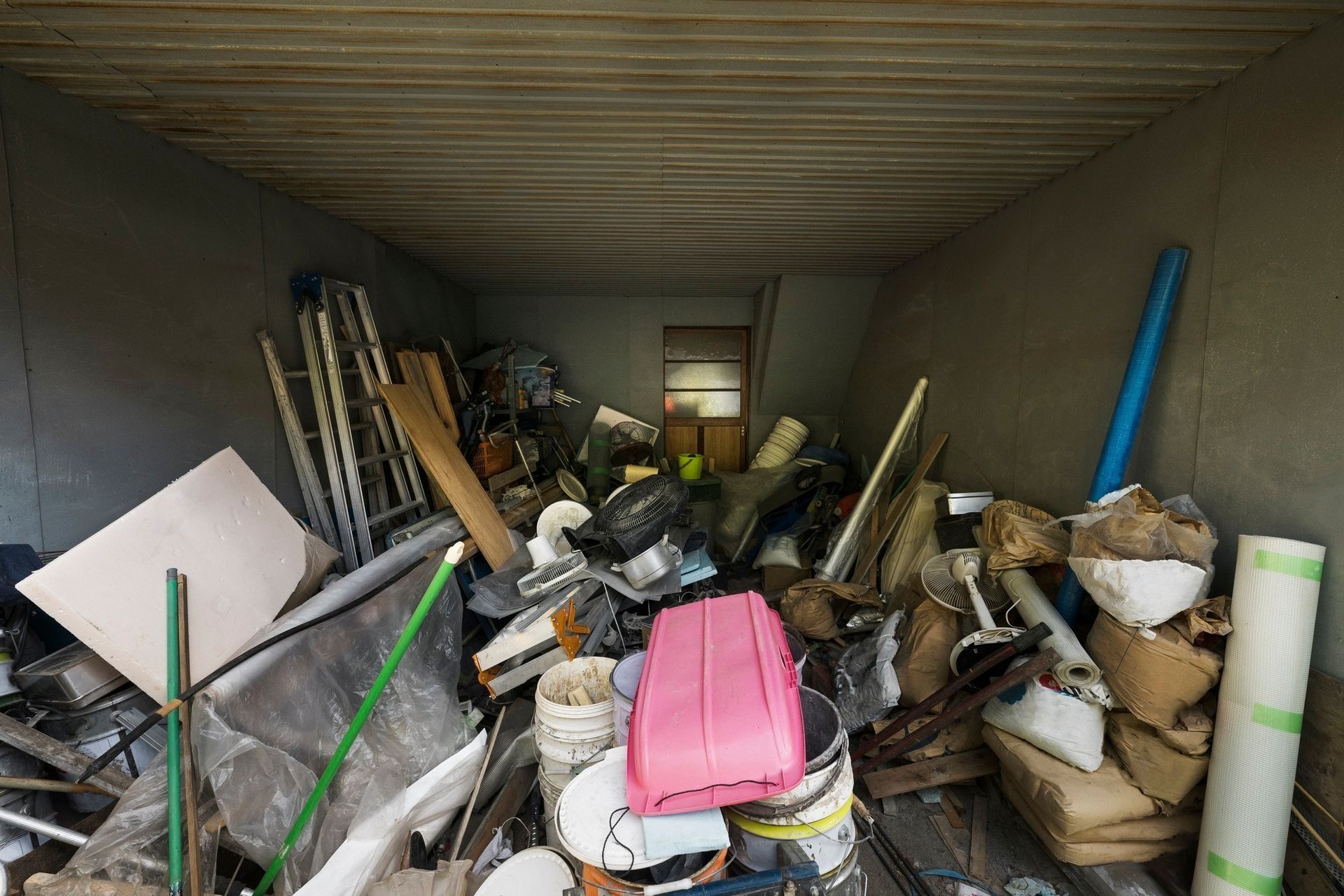 A cluttered storage unit filled with trash, tools, and other items; inside and dark.