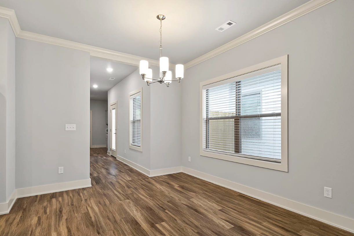 Empty dining room with wood floors, light gray walls, and white trim. Chandelier hangs from ceiling.