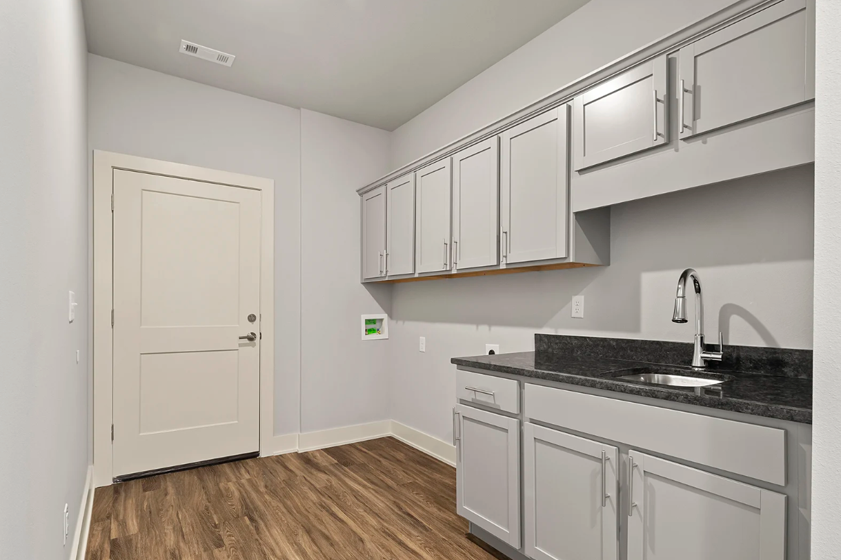 Laundry room with gray cabinets, granite countertop, sink, and closed door.