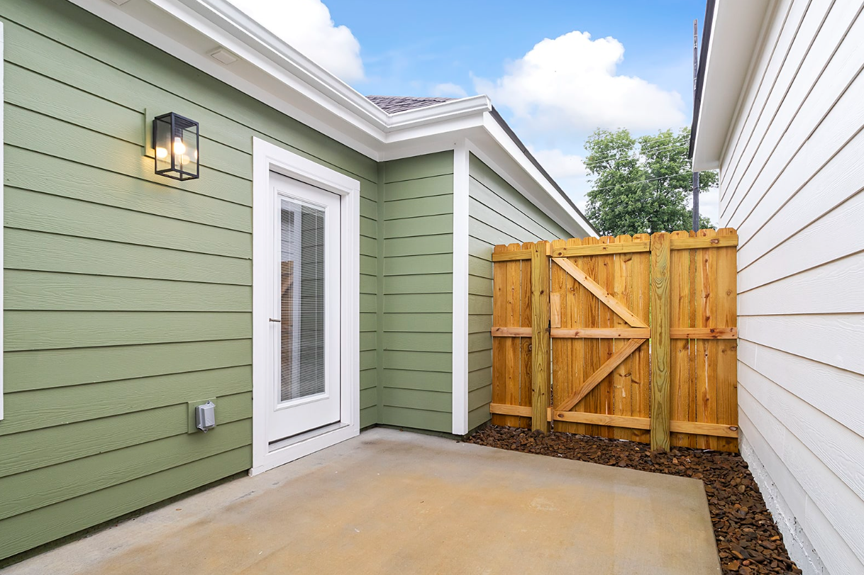 Green-sided house with a small patio, door, and wooden fence.