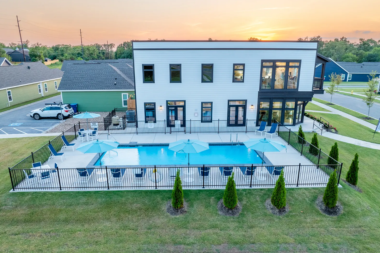 Two-story white building with pool and umbrellas, black fence, and green lawn.