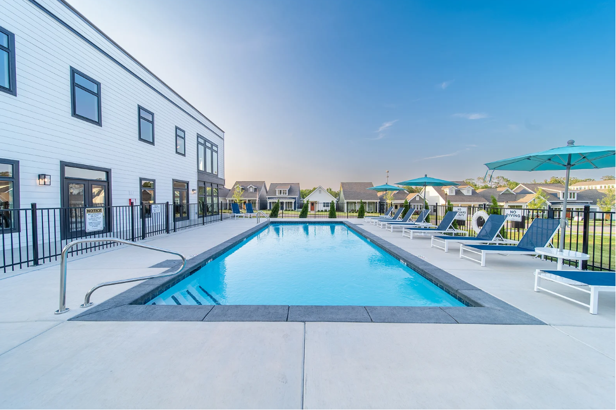 Pool with lounge chairs and umbrellas beside a white building on a sunny day.