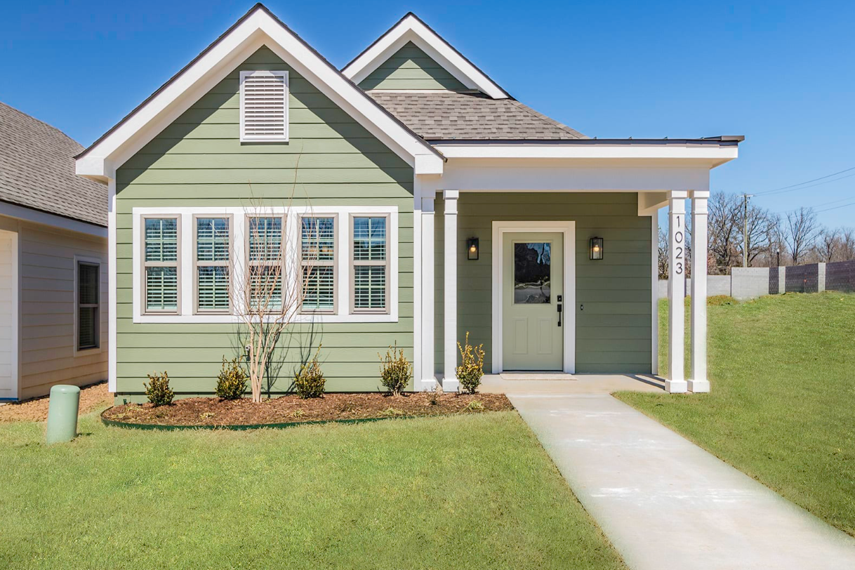 Green cottage with white trim, front porch, and walkway on a sunny day.