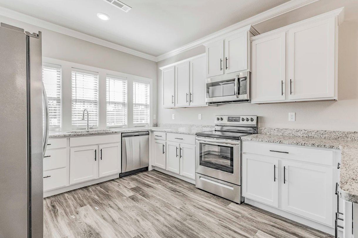 White kitchen with stainless steel appliances, granite countertops, and wood-look flooring.
