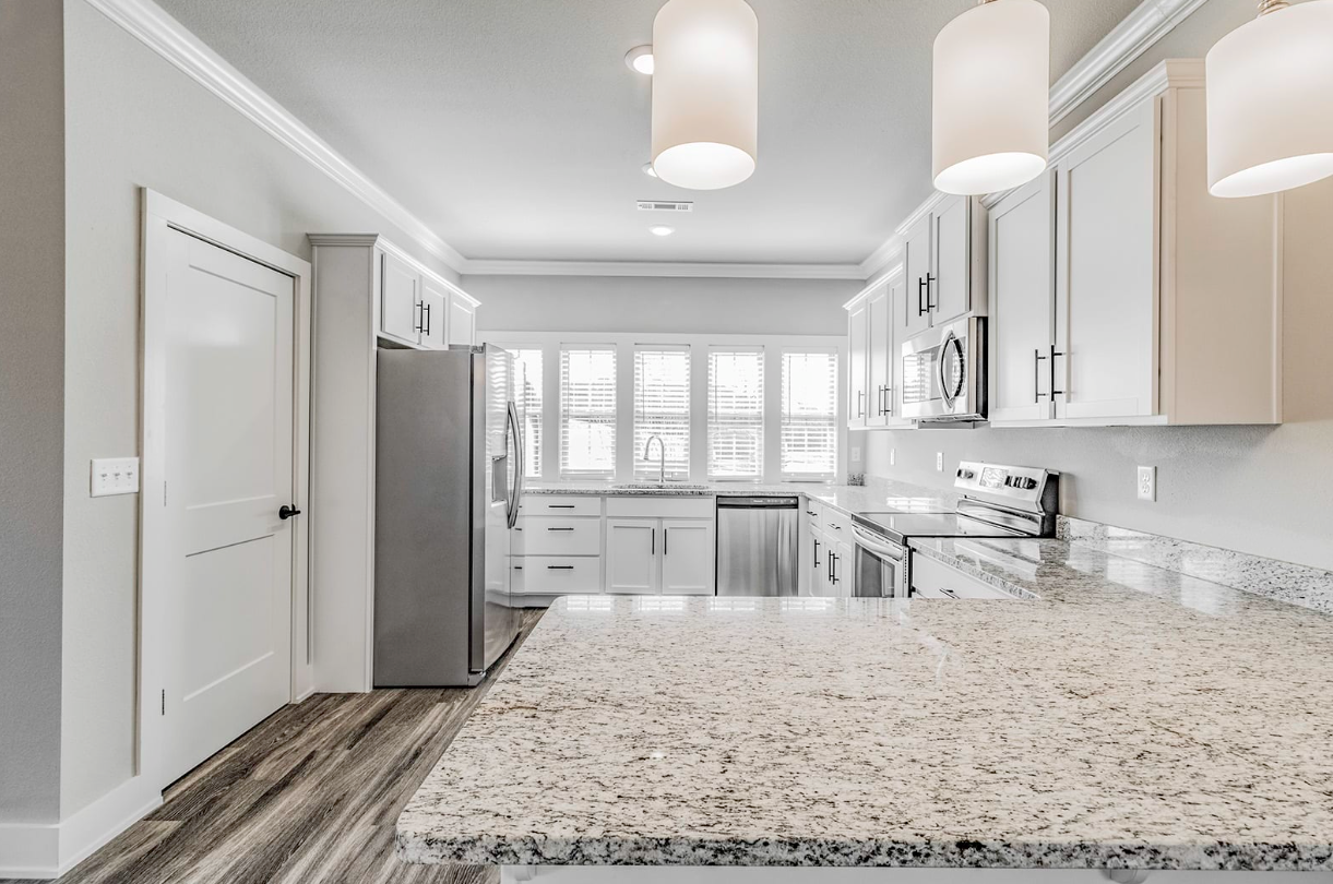 Bright, modern kitchen with white cabinets, stainless steel appliances, and a granite countertop island.