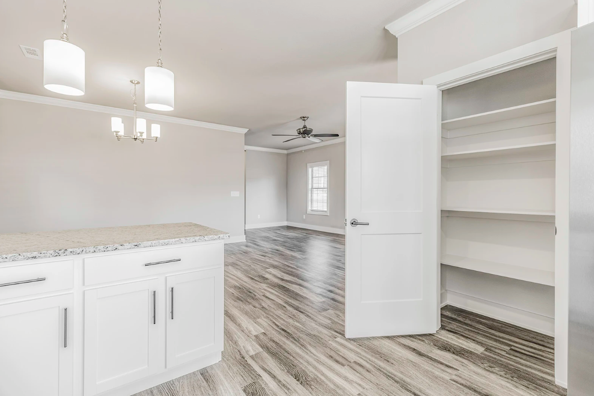 White kitchen with granite counter, pantry, and light wood flooring.