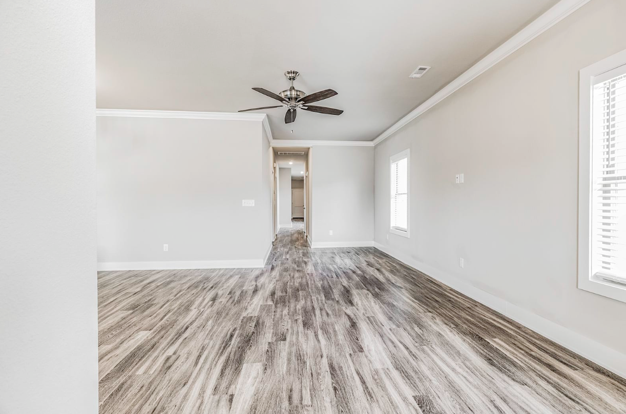 Empty living room with wood-look flooring, white walls, and a ceiling fan.