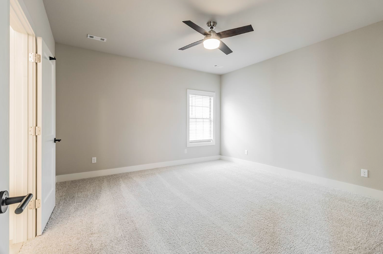 Empty room with light gray walls, white carpet, ceiling fan, and window.