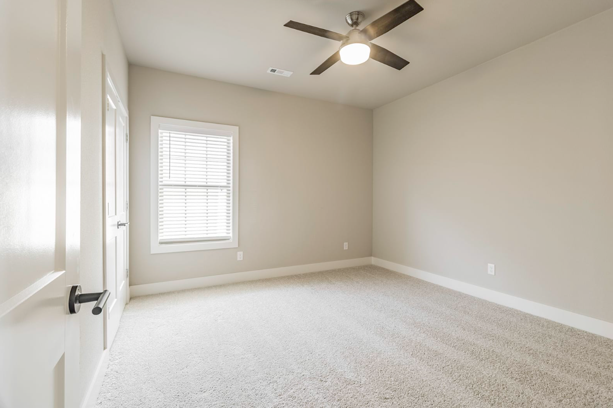 Empty room with beige walls, carpet, window, ceiling fan, and closed door.