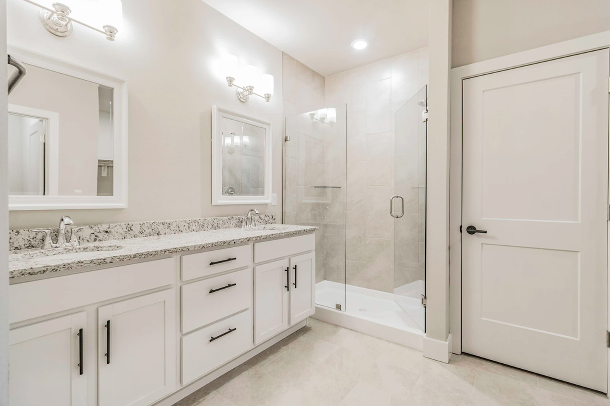 White bathroom with double vanity, walk-in shower, and closed door.