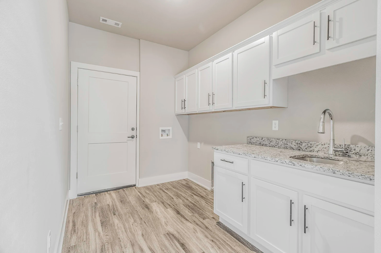 Laundry room with white cabinets, granite countertop, and wood-look flooring.