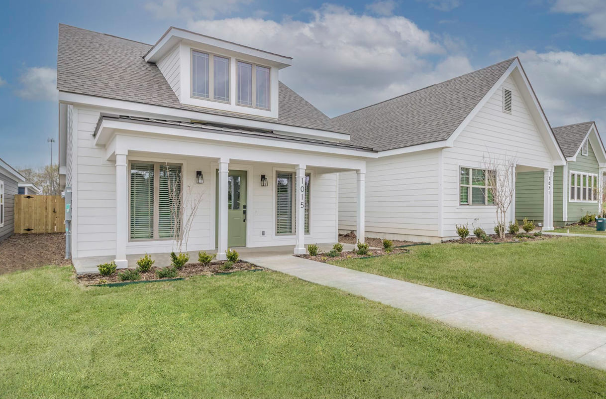 White house with green door and porch, gray roof, walkway on lawn.