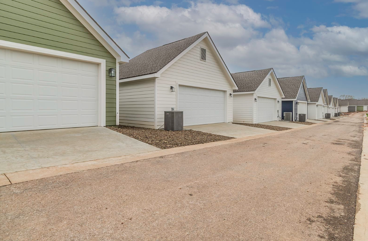 Row of attached garages with white doors and gray roofs, along a gravel road.