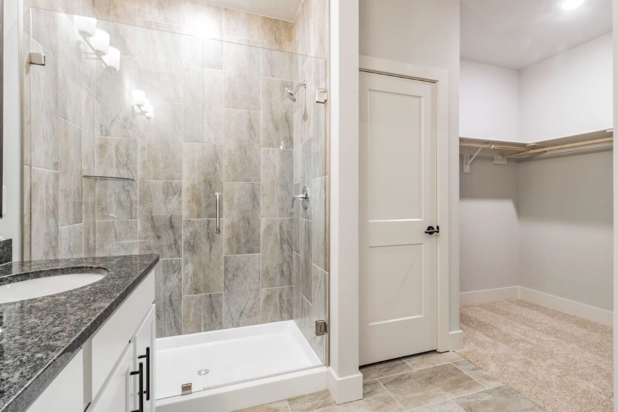 Bathroom with glass shower, double vanity, and walk-in closet with carpet.