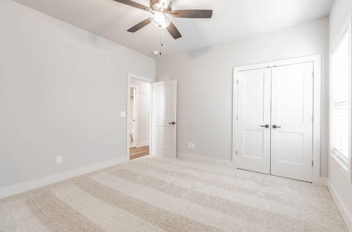 Empty bedroom with light gray walls, a ceiling fan, and striped beige carpet.