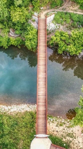 An aerial view of a wooden bridge over a river surrounded by trees.