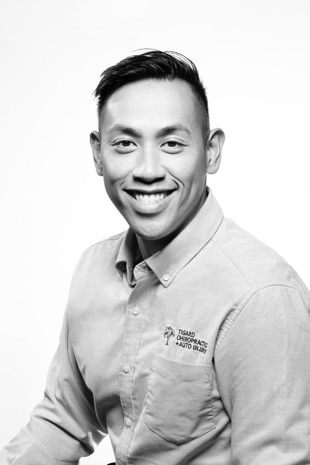 A black and white photo of a smiling man wearing a shirt.