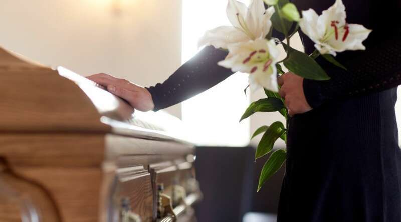 A woman is holding flowers in front of a coffin at a funeral.