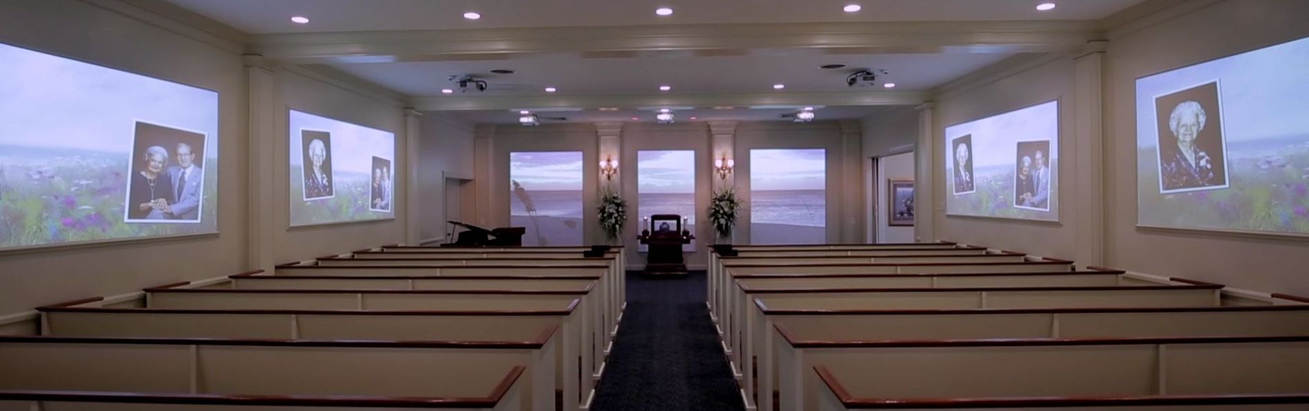 A church with rows of benches and a large screen on the wall.