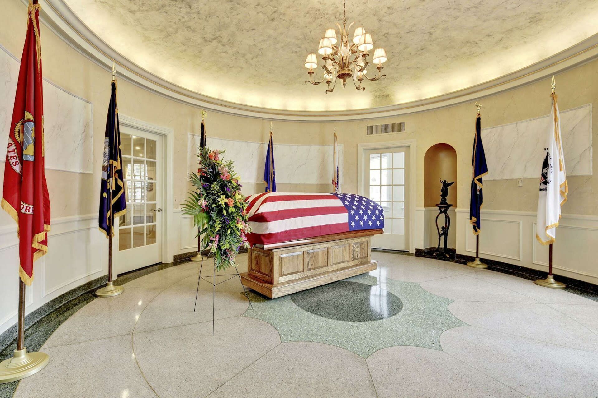 A coffin with an american flag on it is in a room with flags.