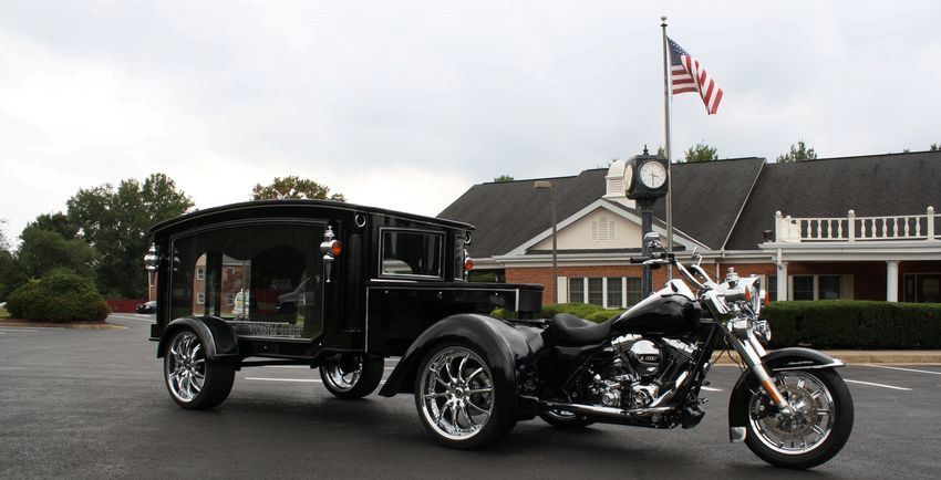 A motorcycle is pulling a black hearse in front of a building